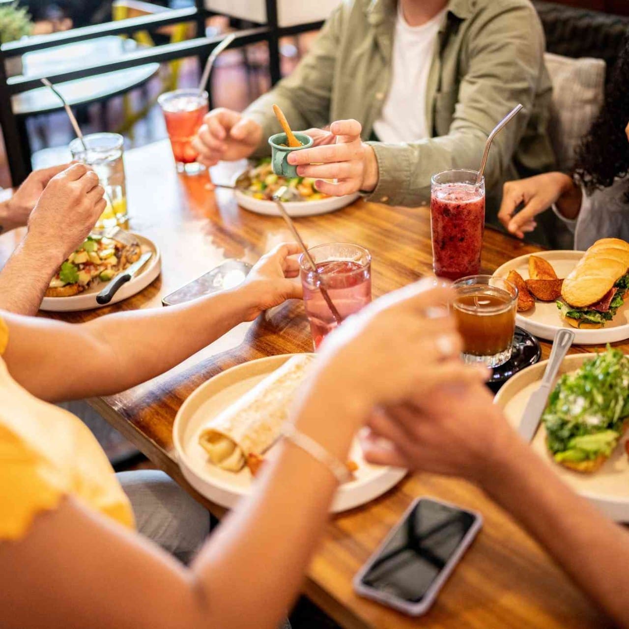 Grupo de adolescentes come en un restaurante. En la mesa hay platos con sandwiches, wraps y tostadas.